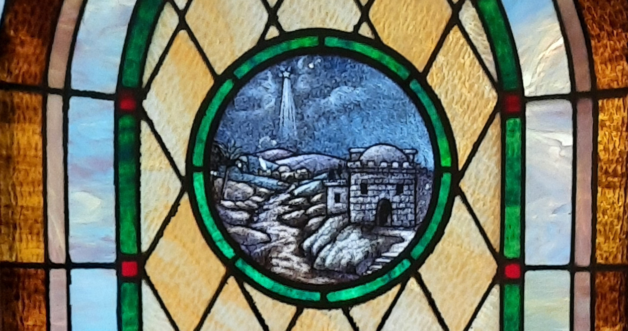Stained glass window with center image of the Christmas star over Bethlehem.