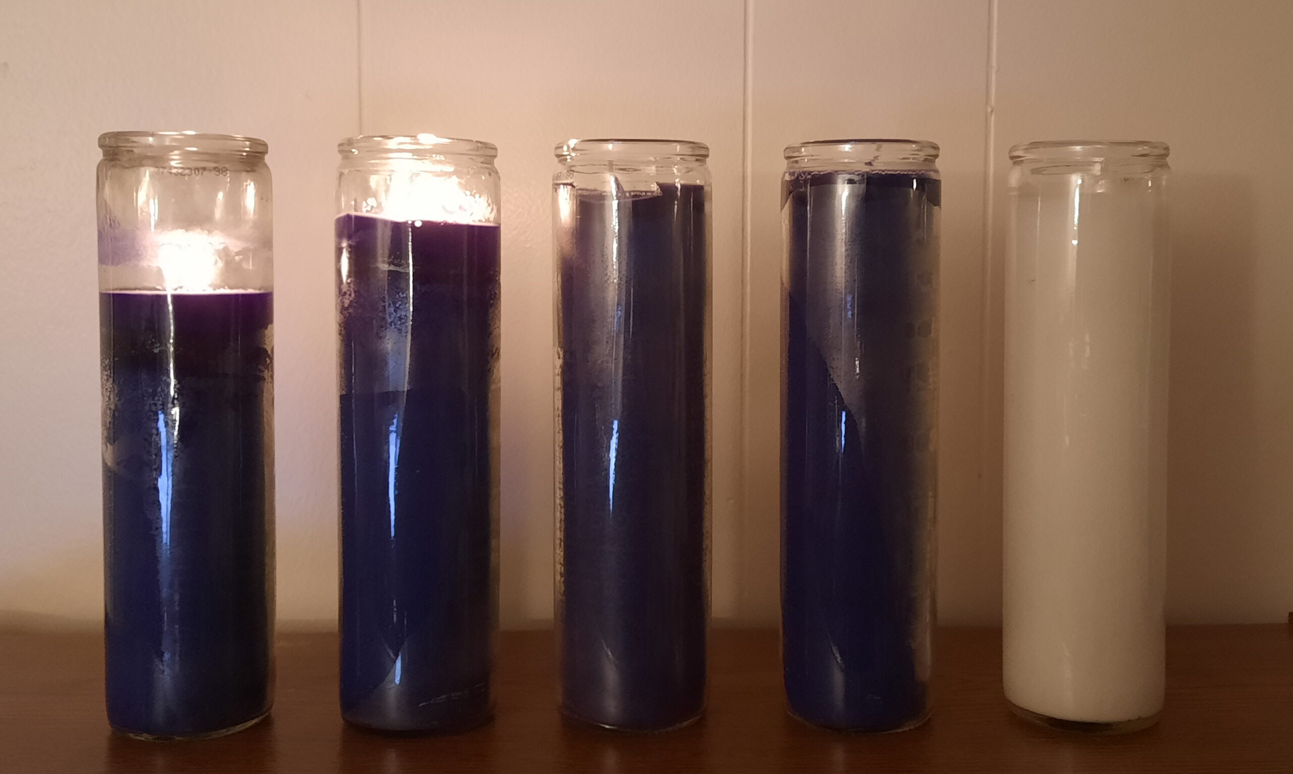 Four purple devotional candles and a white devotional candle. Two of the purple candles are lit.