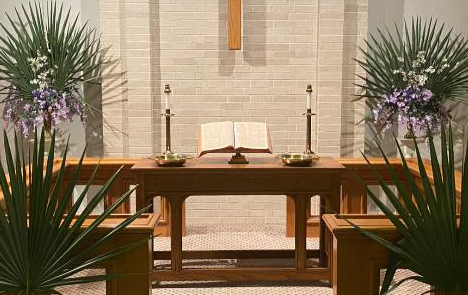 Photo of the altar of China Methodist Church decorated for Palm Sunday in 2022. There are palms in the foreground and a pair of palms in the background, sharing vases with purple and white flowers.
